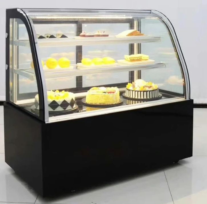 Layaan refrigerated cake display counter with a curved glass front and black base panels, three lit tiers of cakes and pastries inside
